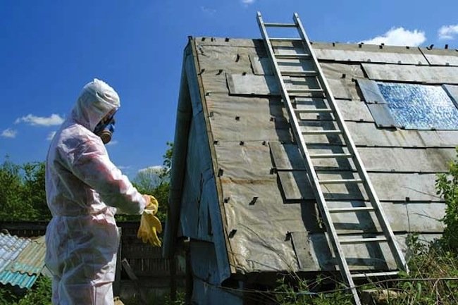 A man in a protective suit standing next to a ladder addressing the dangers of asbestos.