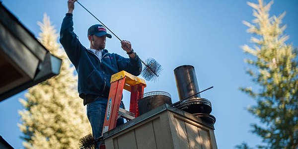 A man performing maintenance on a ladder, cleaning a chimney.
