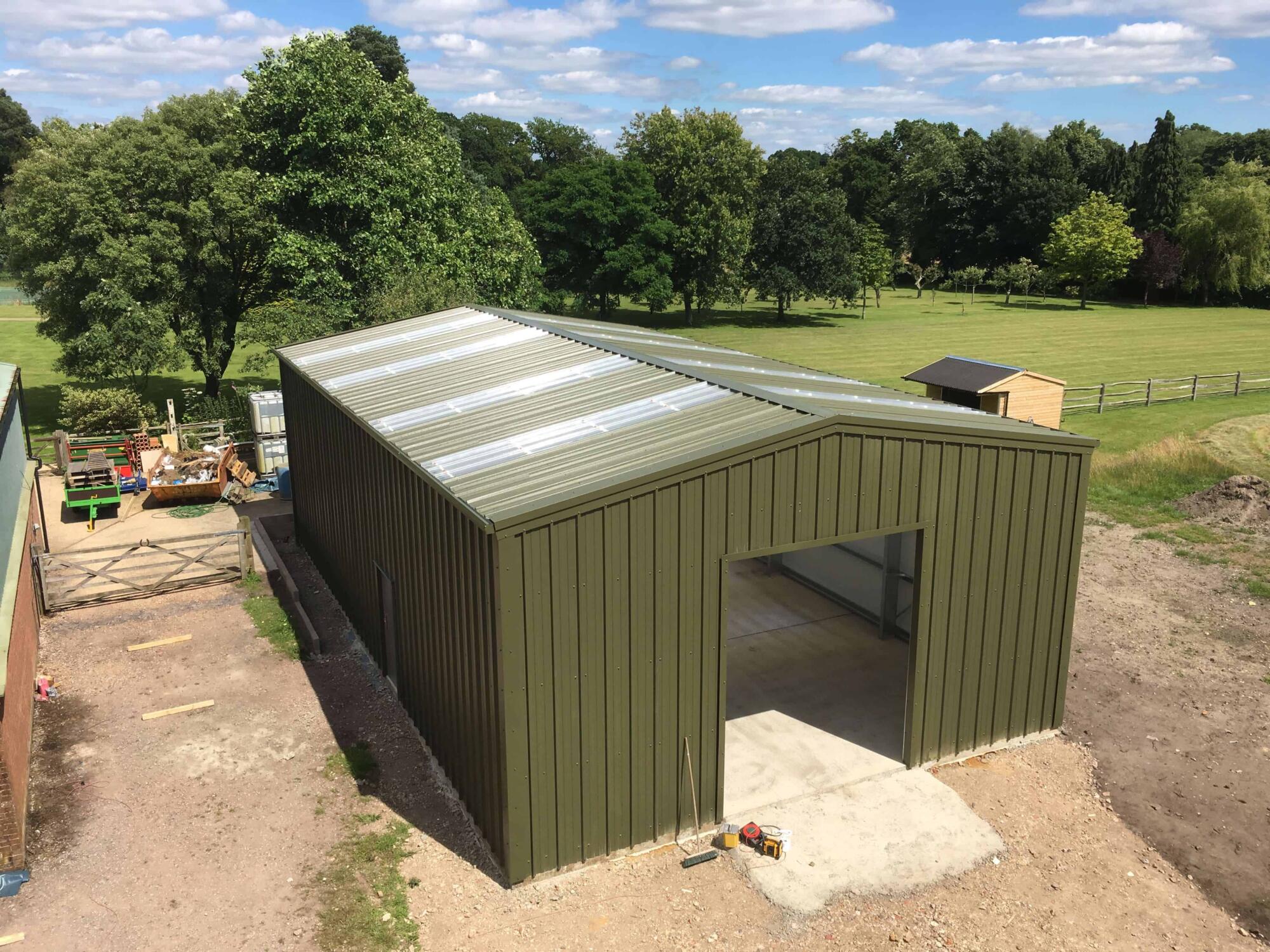 An aerial view of a green shed in a field constructed with steel buildings.