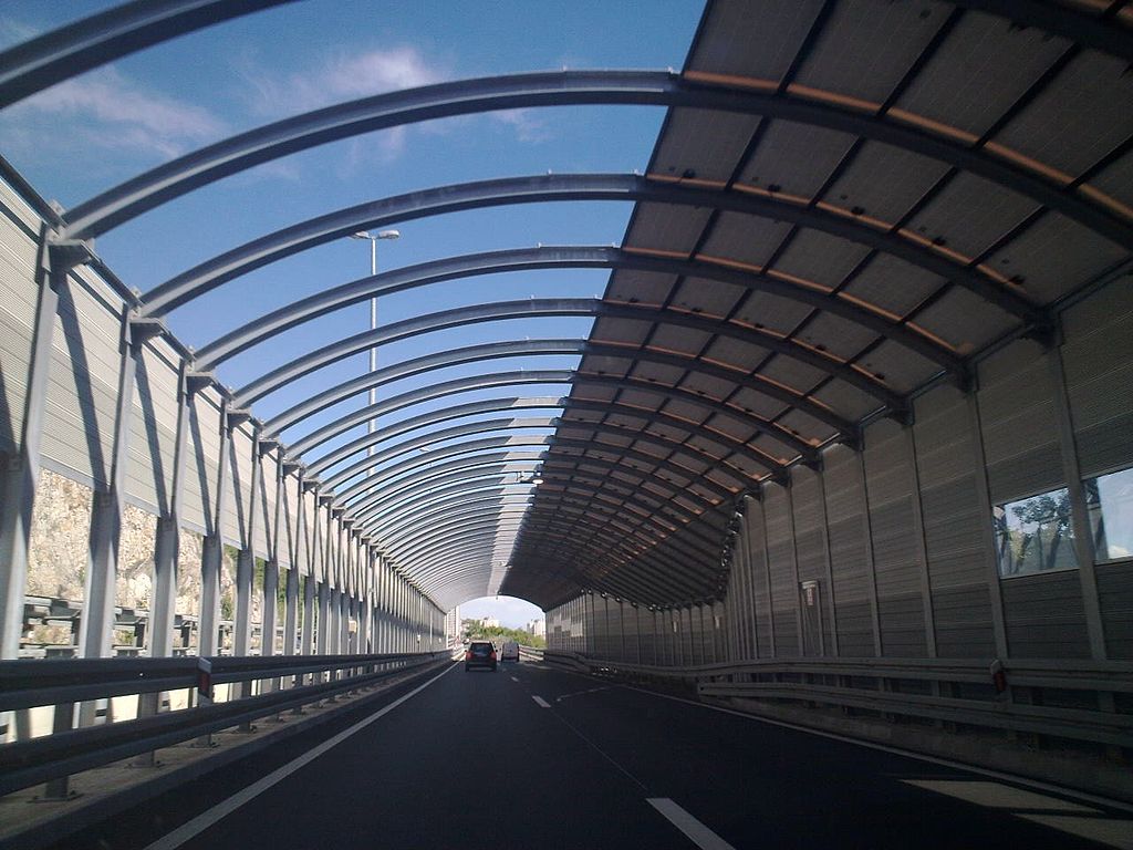 A car is driving down a highway with an acoustic barrier in a tunnel.