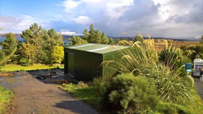 A green shed on a dirt road next to a lake, now made of steel.