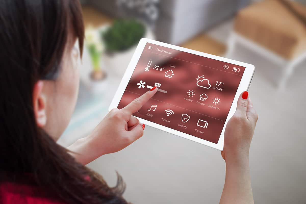 A woman is pointing at a tablet with home technology icons on it.