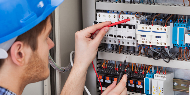 A commercial electrician in a hard hat is working on an electrical panel.