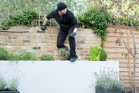 A man in a black hoodie climbing a wall to protect a garden.