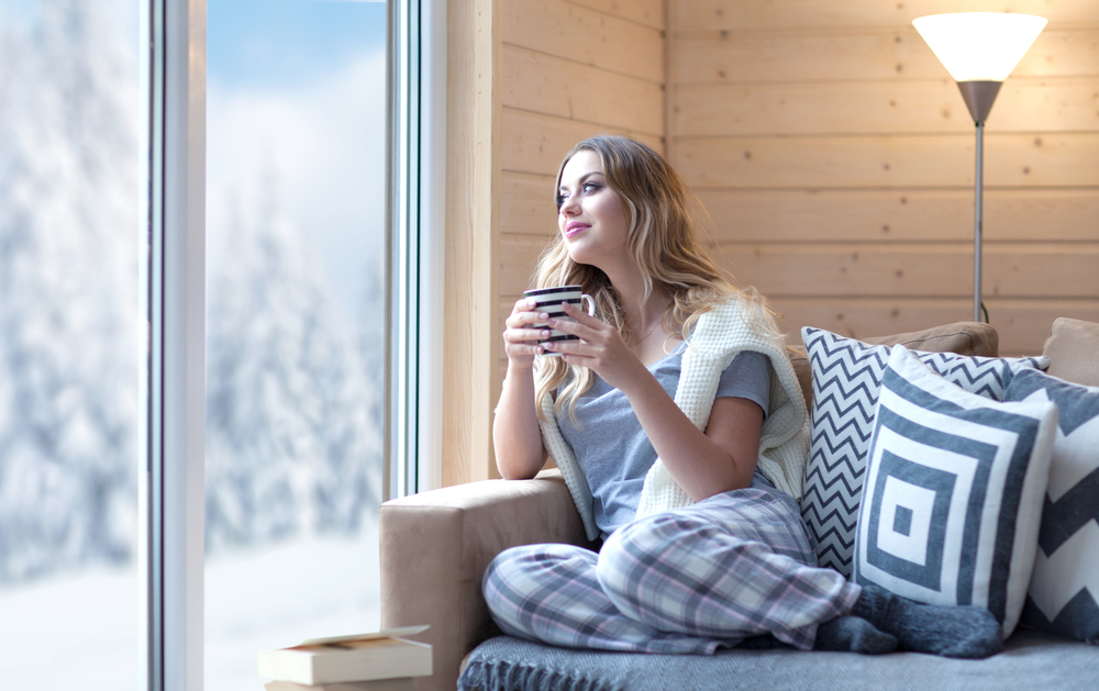 A woman sitting on a couch with a cup of coffee in the winter season.