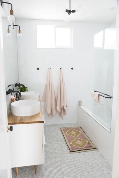 A pink rug and white sink beautifully complement the white bathroom design.