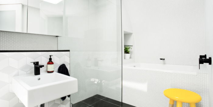 A white bathroom with yellow stool and bathroom tiles.