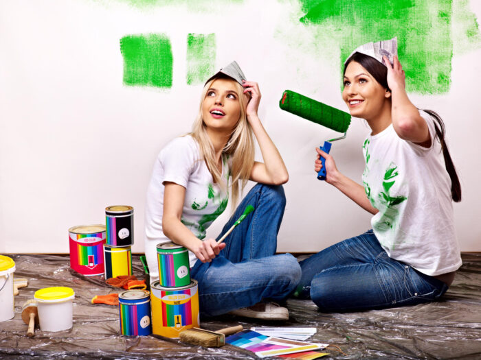 Two women debunking home staging myths while painting a room with green paint.