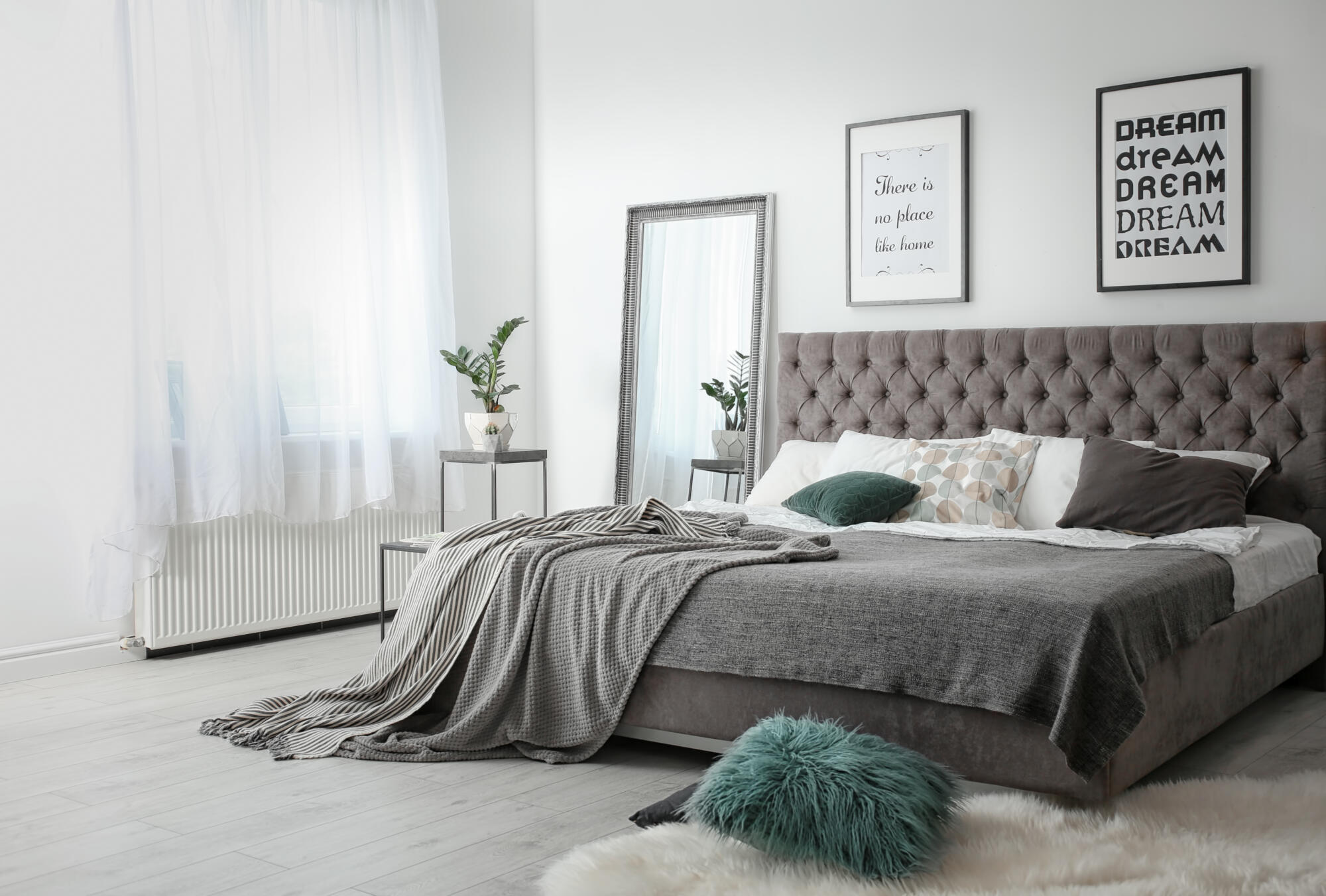 A minimalist bedroom design with a grey bed and green pillows.