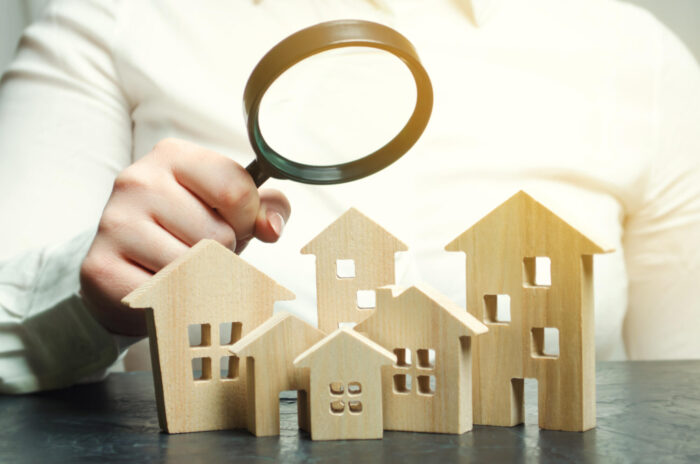 A woman is holding a magnifying glass over a wooden houses. Real estate appraiser.