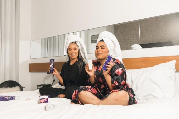 Two women sitting on a teen bedroom bed with towels on their heads.