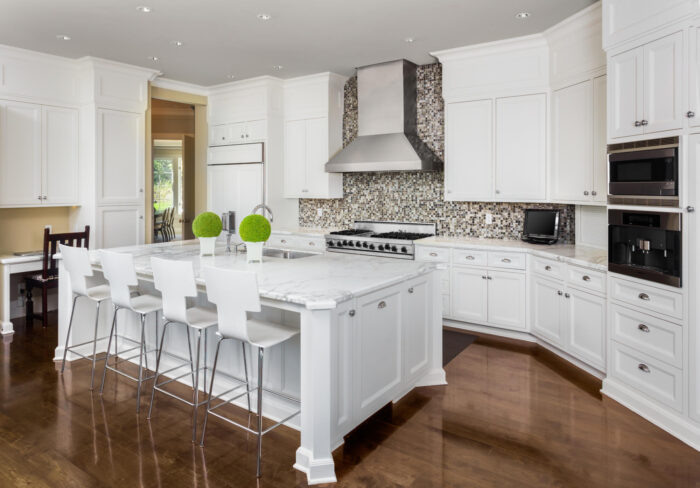 A white kitchen with a center island and bar stools, featuring a kitchen peninsula.
