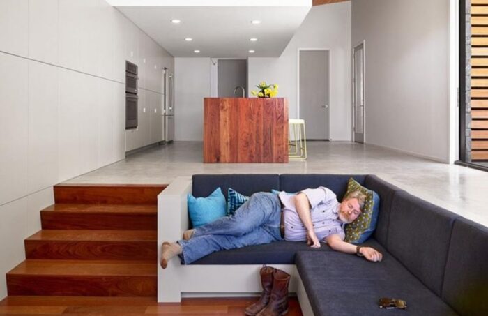 A man is sleeping on a couch in a sunken living room.