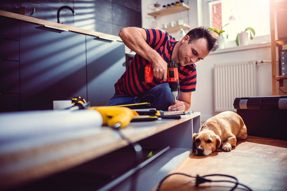 A man ensuring drilling safety while working on a project with his dog on the floor.