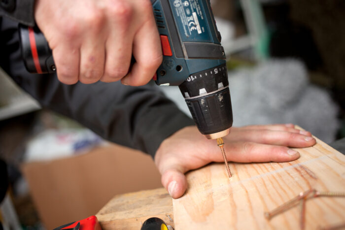 A person practicing drilling safety on a piece of wood.