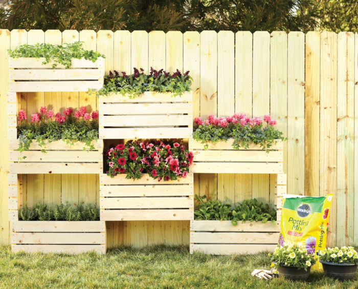 A wooden planter with flowers on it in front of a fence in a hanging garden.