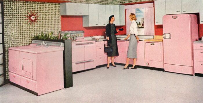 Two women, one wearing a pink outfit, standing in a kitchen.
