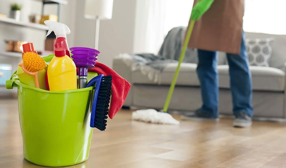A man disinfecting a living room with a bucket full of cleaning supplies.
