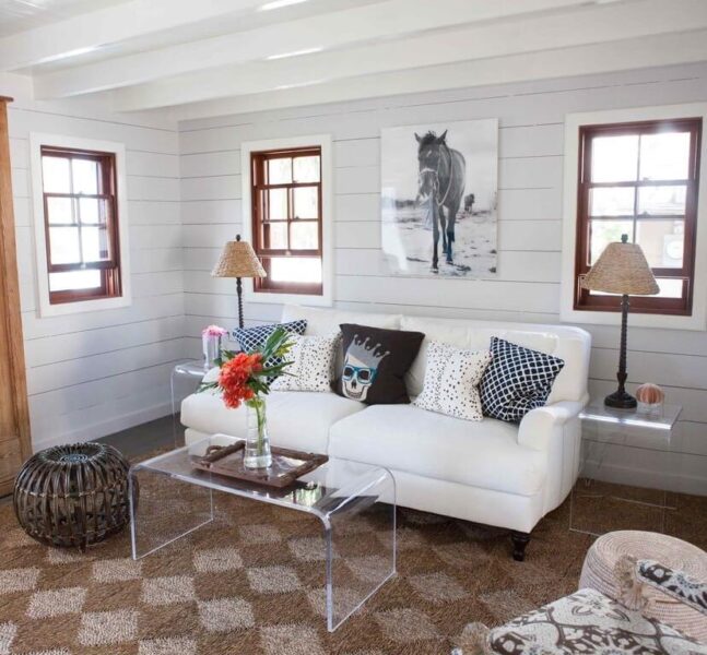 A beach themed living room with a white couch and a glass coffee table.