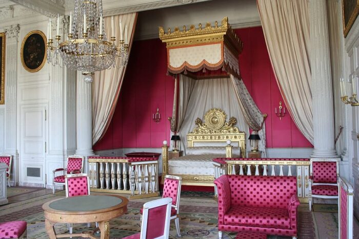 A large room with a bed, chairs, and a pink chandelier.