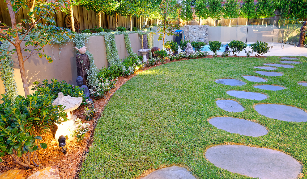 A landscaped backyard with stepping stones and a lawn.