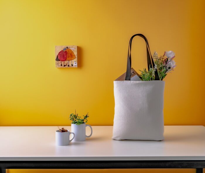 A white tote bag sitting on a table next to a cup of coffee in a vegetable garden.