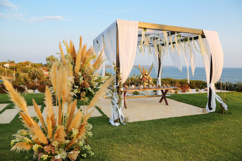 A wedding ceremony set up on a grassy area near the ocean with pampas grass as decoration.