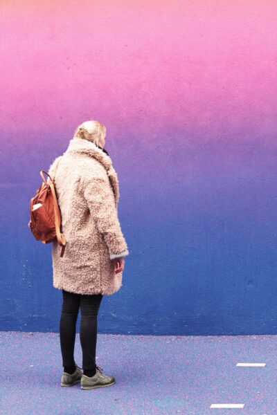 A woman in a brown coat standing in front of a colorful wall showcasing various color schemes.