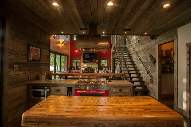 A cozy kitchen with a wood stove and stairs, featuring rustic design elements.