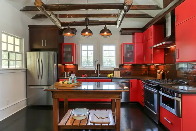 A rustic kitchen with red cabinets and black counter tops.