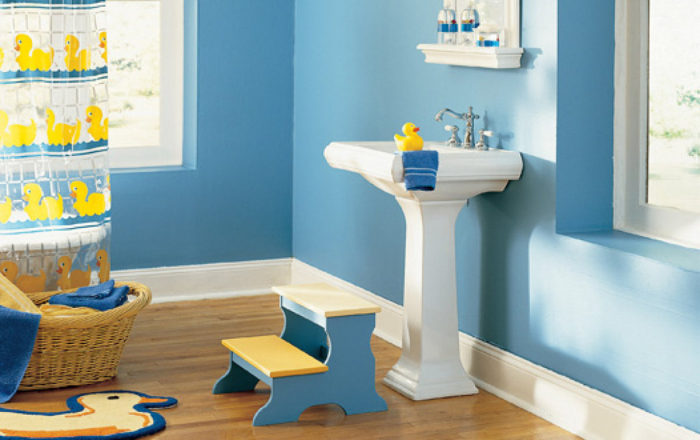 A kids bathroom with blue walls and a yellow stool.