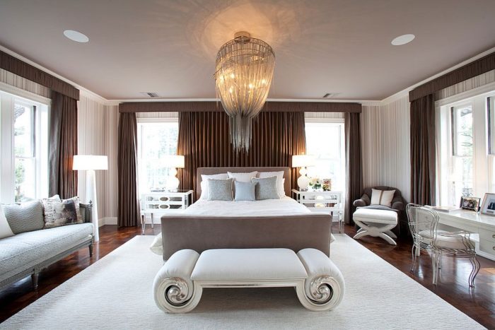 A white bed in a bedroom illuminated by a chandelier.
