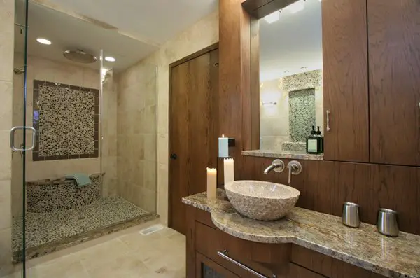 A modern basement bathroom with granite counter tops and a glass shower.