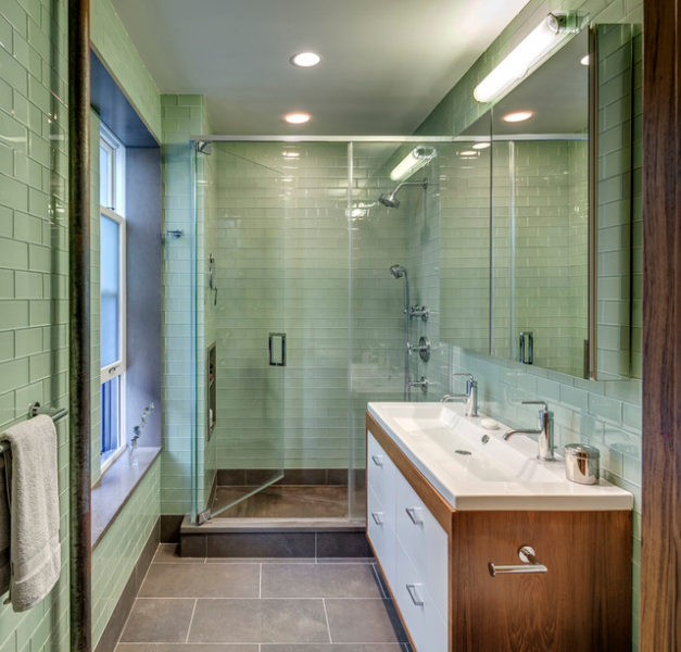 A bathroom with green tiles and a glass shower stall.