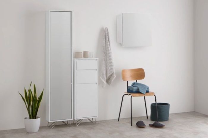 A white bathroom with a mirror, a chair, and ample storage space.