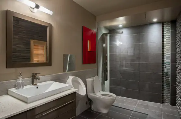 A modern basement bathroom with grey tile and a toilet.