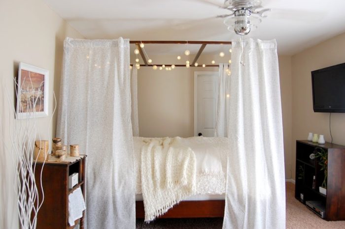 A white canopy bed in a bedroom with string lights.
