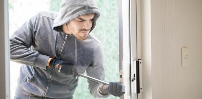 A man in a hoodie opening a door with a knife, reminding you to protect your home while on vacation.