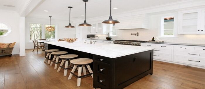 A black and white kitchen with a center island and stools, featuring indoor lighting.