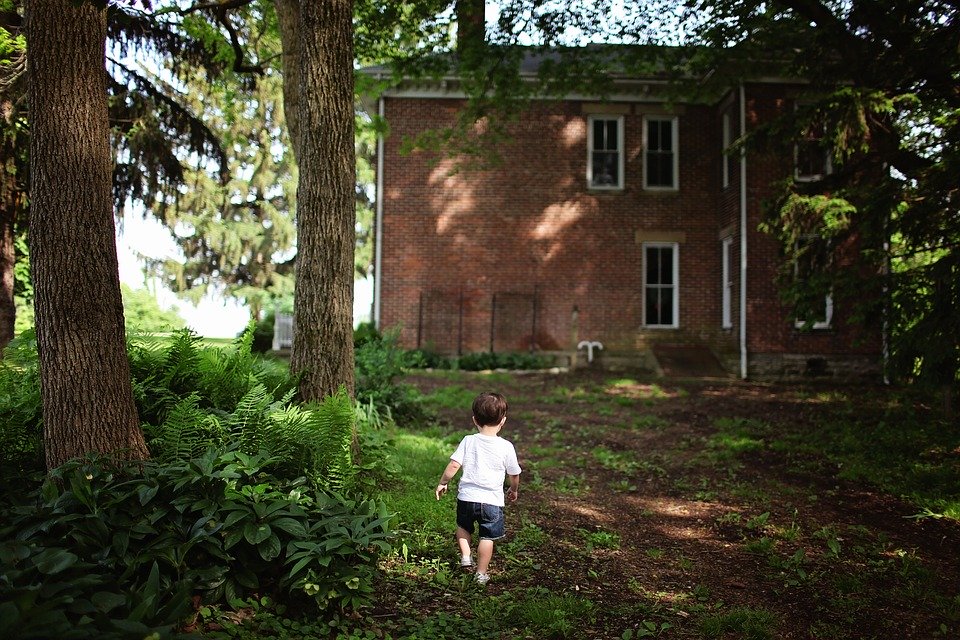 A boy walks past a brick house in the woods, creating a cohesive and welcoming atmosphere in the large yard.