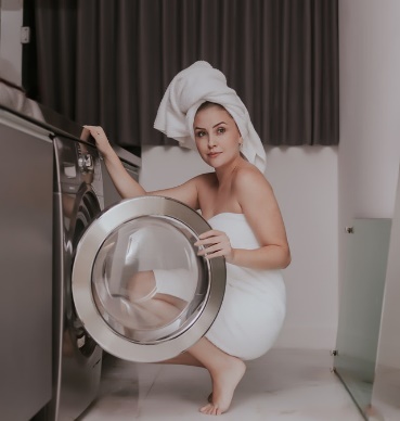 A woman in a towel crouching next to a washing machine demonstrates how to stop shortening the life of your washing machine.