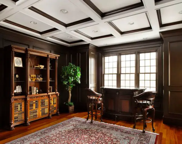 A home office with wood paneling and a rug, featuring a dining room ceiling.