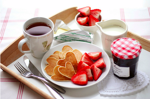 A romantic breakfast with pancakes, strawberries, and a cup of milk.