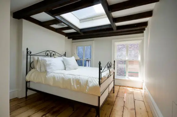 A bed in a room with wooden floors and a skylight located under a dining room ceiling.