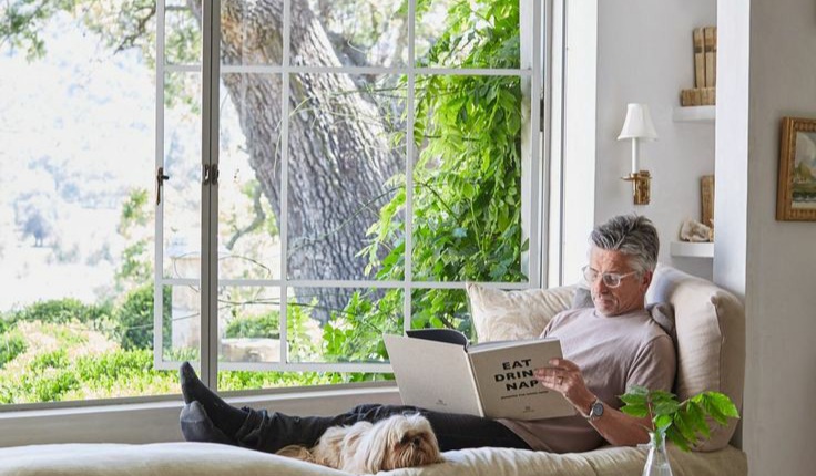 A man reading a book on a couch in front of new windows.