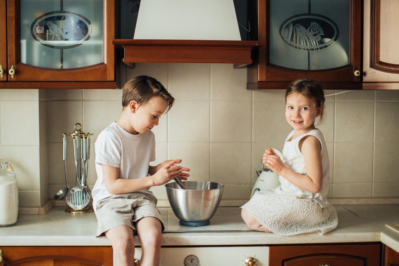 Two children are mixing ingredients in a bowl in the kitchen while practicing safety measures.