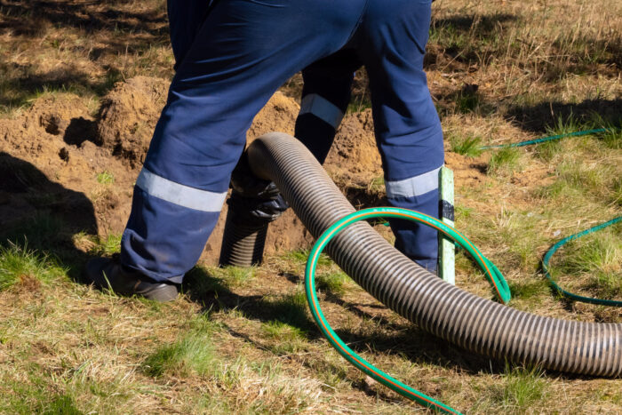A man using a hose in a field while working on trenchless sewer repair.