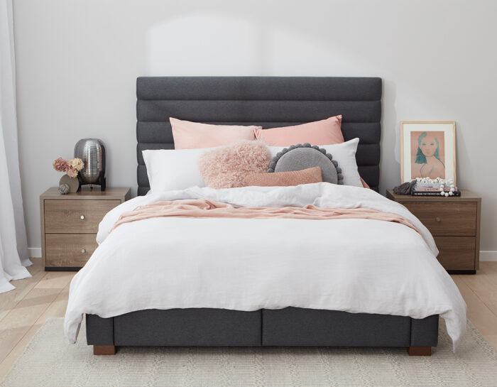 A comfortable bed with a grey headboard and pink pillows.