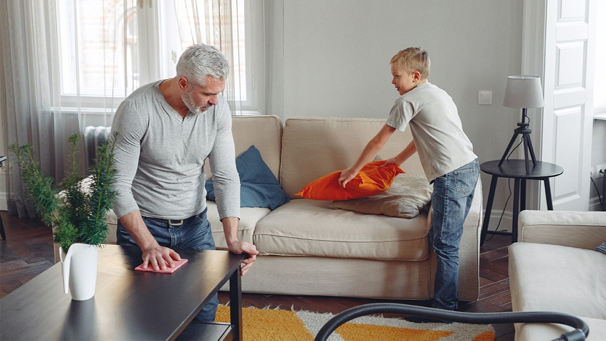 A man and a boy tidying a home's living room for a safe environment.