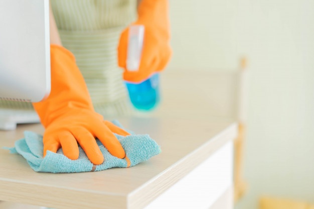 A woman in orange gloves cleaning a home desk.